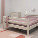 Ein weißes Einzelbett „FLEXA“ aus der CLASSIC-Kollektion in einem minimalistisch eingerichteten Kinderzimmer mit rosa Bettwäsche, Kommode und Teppich.