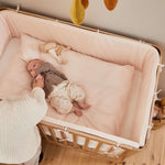 Femme à côté dun lit bébé FLEXA de la collection OAK, finition bois clair, dans une chambre denfant où lon aperçoit les bords arrondis, sans danger pour les enfants.