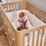 Bébé avec une tétine dans un lit bébé FLEXA, en chêne, avec literie moelleuse et tours de lit, chambre denfant ; barrières de sécurité visibles.