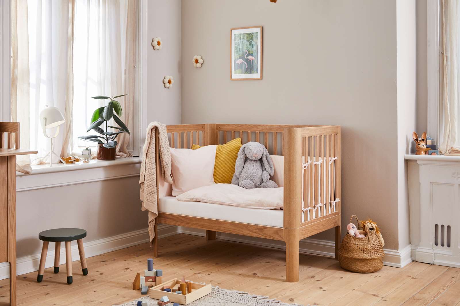 Lit bébé FLEXA BABY en chêne dans une chambre denfant aux tons neutres, avec une literie douillette et des bords arrondis pour la sécurité de lenfant.
